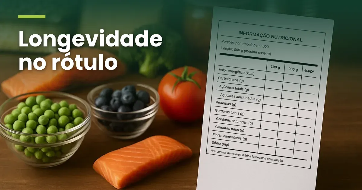 Mesa de madeira com dois filés de salmão, uma tigela de ervilhas, uma de mirtilos, brócolis, tomate, embalagens e um pote ao fundo. À direita, um cartão branco inclinado traz a tabela de informação nutricional no modelo vertical, em branco: porções e porção com 000, colunas 100 g, 000 g e %VD e as linhas de valor energético a sódio, sem nenhum valor preenchido, com o título Longevidade no rótulo no alto, em letras brancas sobre um degradê verde
